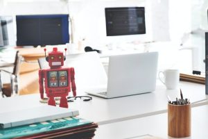 Desktop with a laptop computer and red robot figurine.