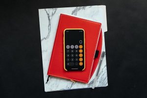 Mobile with calculator app on display on top of a red notebook.