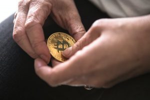 Person holding a gold coin labeled with the bitcoin symbol.